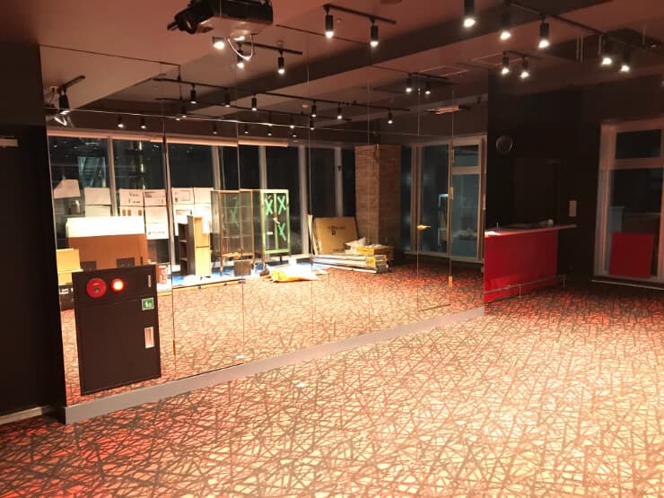 鏡張りの壁と赤茶色の模様入りカーペットが敷かれた、広々とした室内空間。