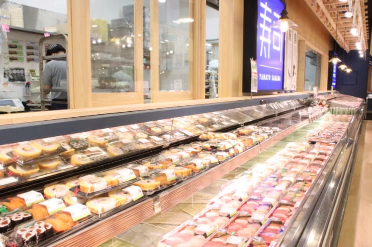 冷蔵ケースに寿司や惣菜が並ぶ店内の様子。「新 YAMATO SAKANA」の文字が見える。