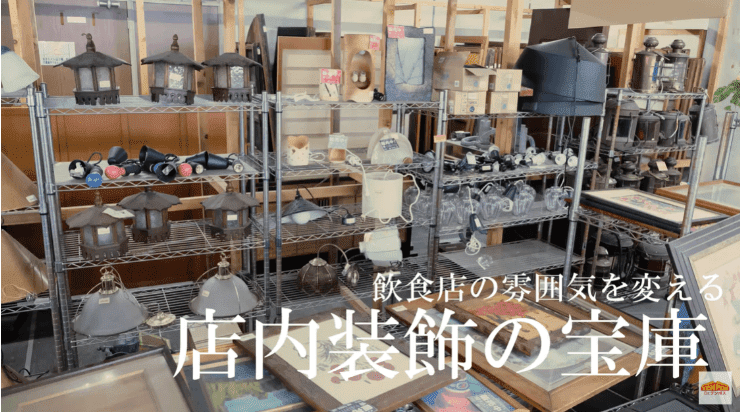 「飲食店の雰囲気を変える 店内装飾の宝庫」と書かれた看板が置かれた、飲食店向けの装飾品が並べられた店内の様子。棚には提灯や照明器具、食器などが陳列されている。