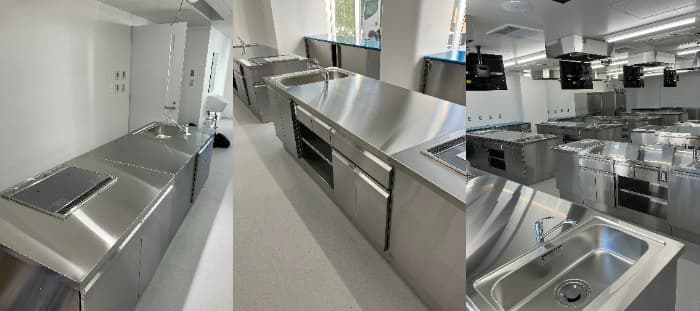 ステンレス製の調理実習台が設置された、清潔感のある実習室の写真です。中央にシンクとIHクッキングヒーターを備えた調理台が並び、右側の写真では換気設備も確認できます。全体的にモダンでプロフェッショナルな雰囲気です。