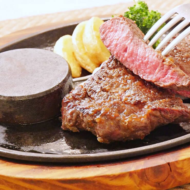 鉄板の上で提供されるステーキのアップ。一口大に切られたミディアムレアの肉がフォークで持ち上げられています。