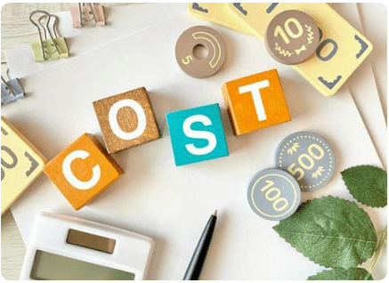 「COST」と書かれた積み木、電卓、ペン、硬貨に見立てた木製コインなどが写っている。費用の検討や経費を象徴する画像。